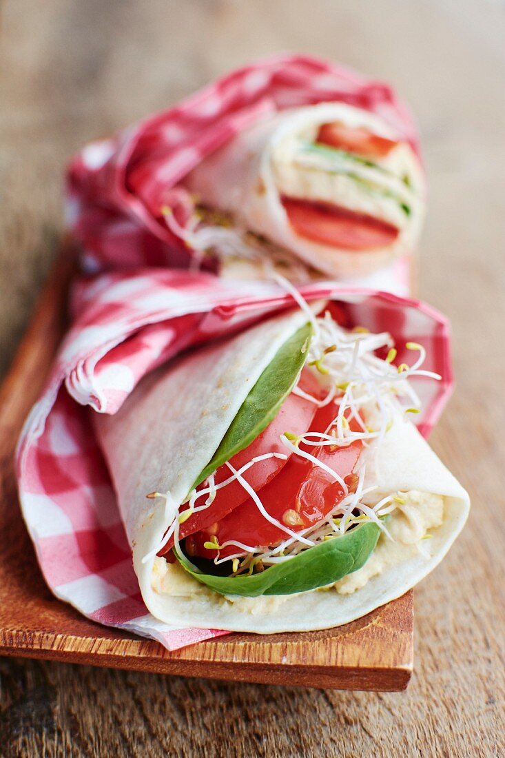 Tortilla wraps with humus, spinach, bean sprouts and tomato slices on a wooden board