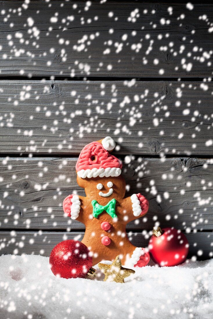 A gingerbread man and Christmas tree baubles with falling artificial snow