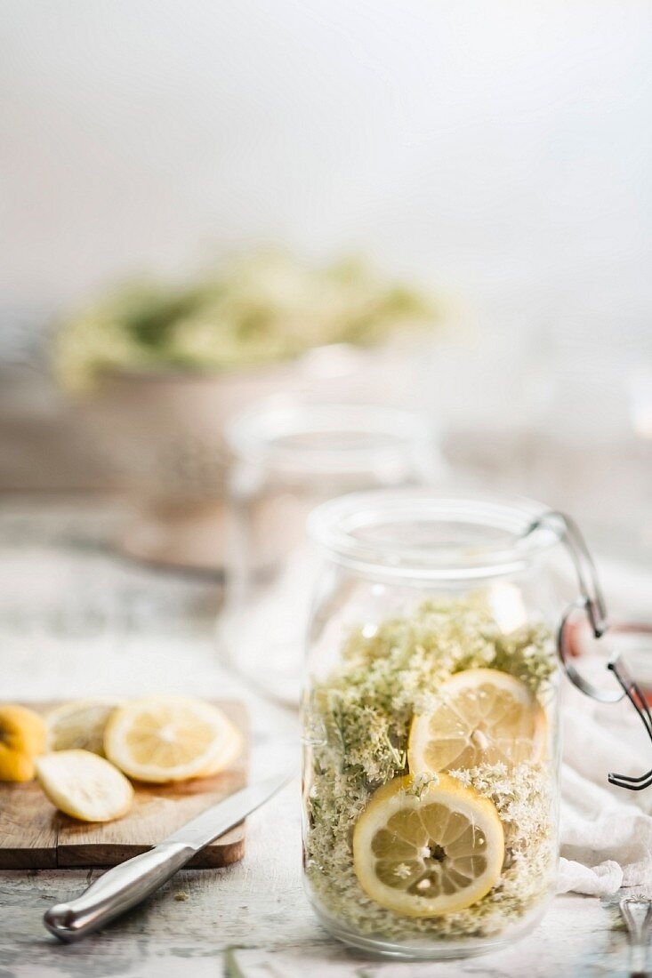 Einmachglas mit Holunderblüten, Zitronenscheiben und Zucker für die Herstellung von Holunderblütenlimonade