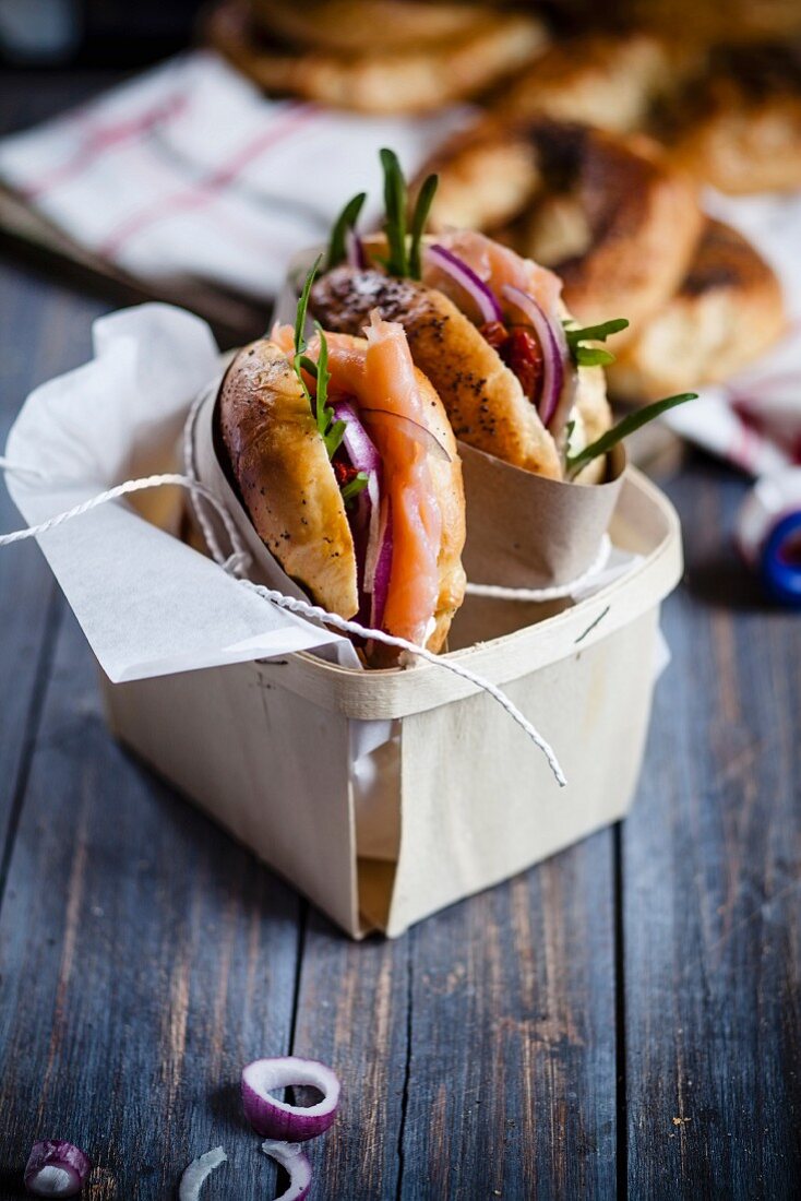 Bagels mit Räucherlachs, Rucola und Zwiebeln, in Papier eingewickelt, im Spankorb