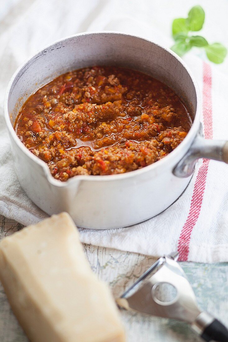 Bolognese sauce in pot with Parmesan cheese next to it