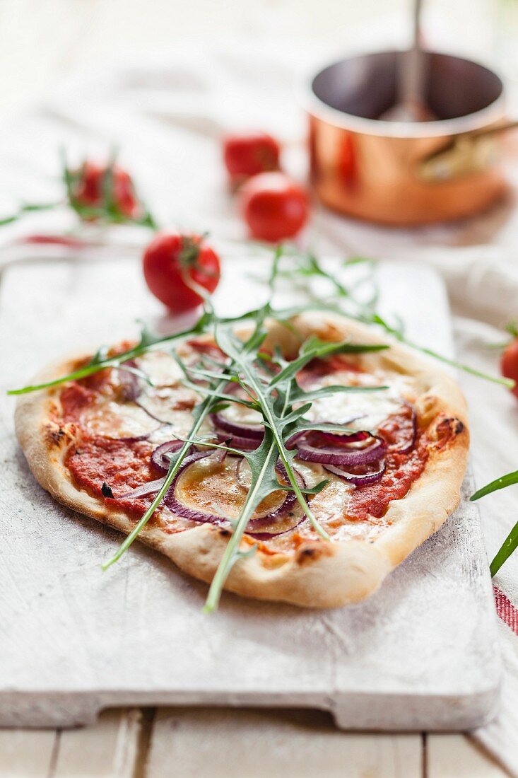 Selbstgemachte Pizza mit Zwiebeln und Rucola auf Schneidebrett