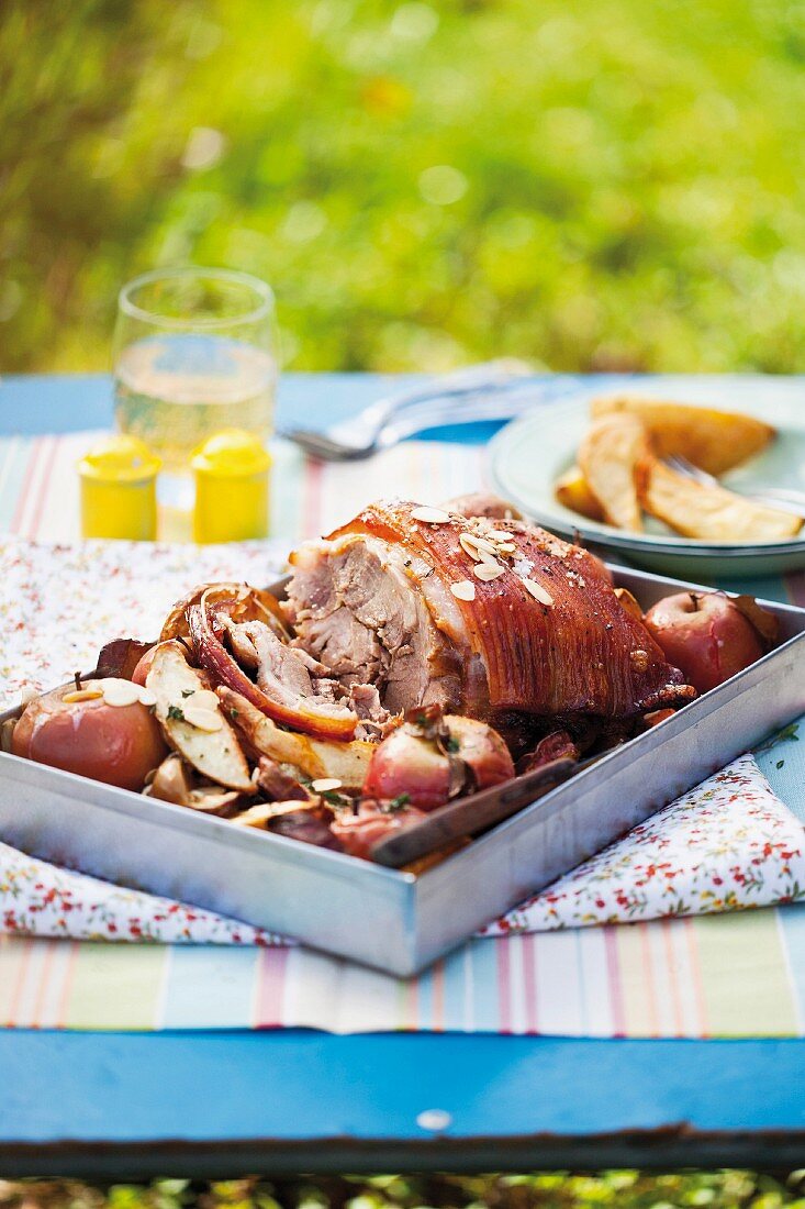 Schweinerollbraten mit Äpfeln auf Tisch im Garten