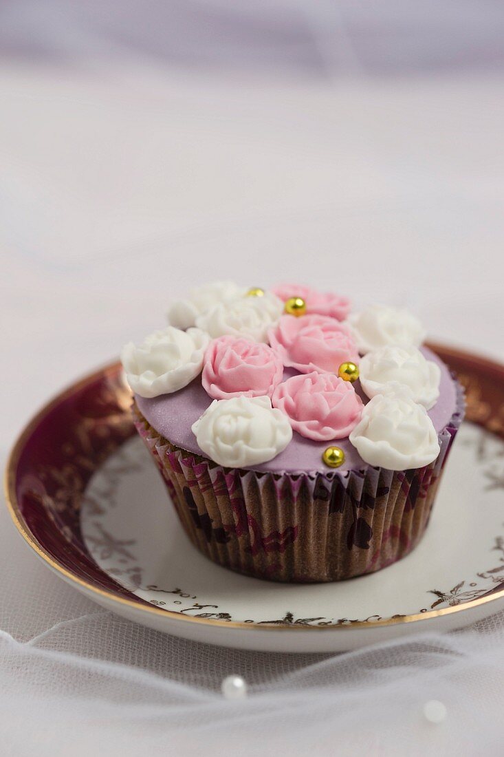A cupcake decorated with rose petal fondant and golden pearls