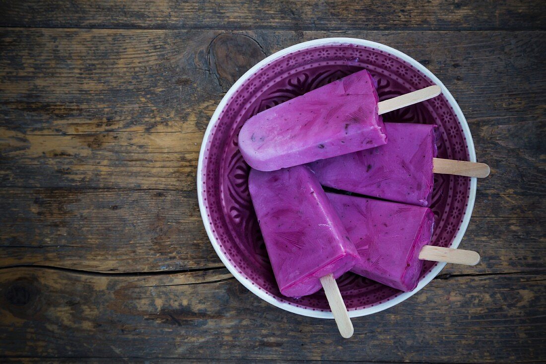 Four yoghurt and blueberry ice lollies on a wooden table (seen from above)