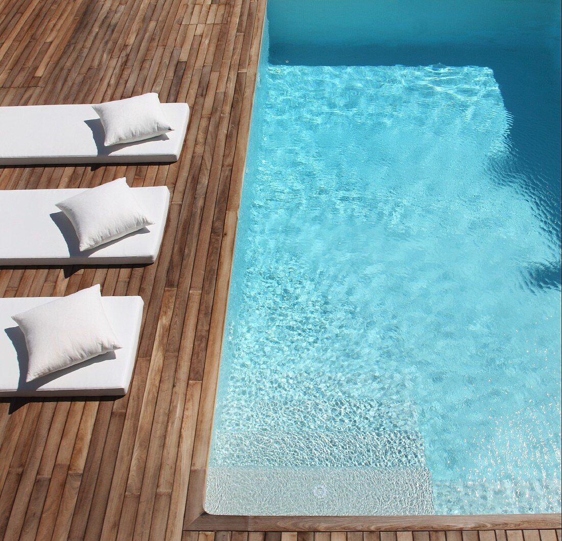 Pale futon loungers with matching cushions on wooden deck adjoining pool