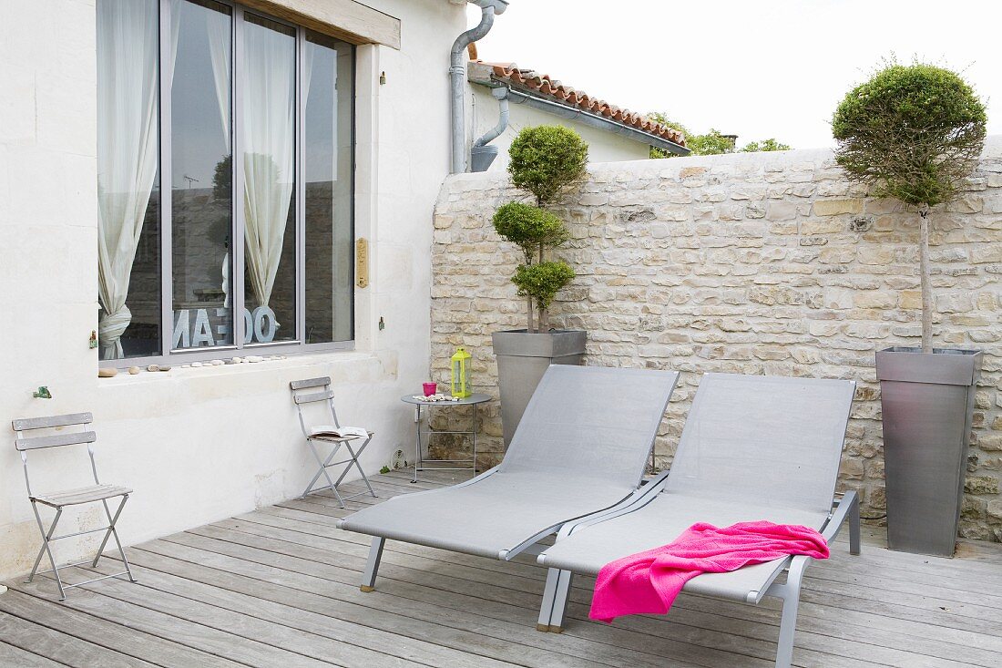 Modern loungers on terrace with wooden deck and stone wall