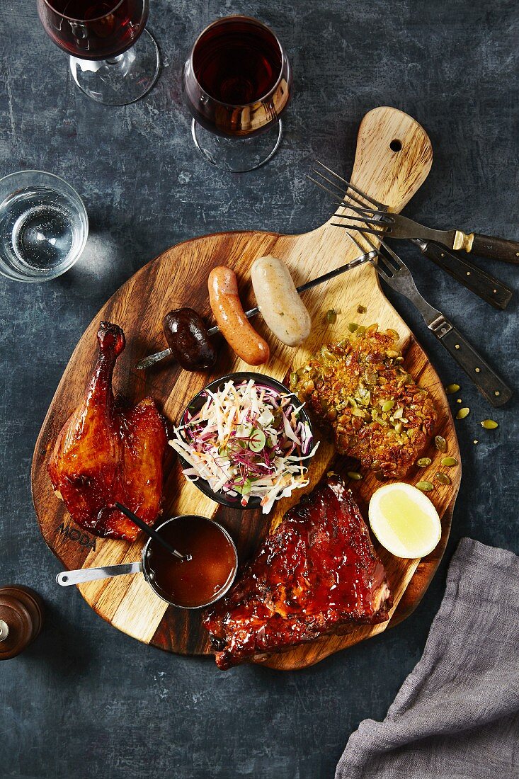 Grilled meats, sauces and a sausage skewer on a wooden chopping board