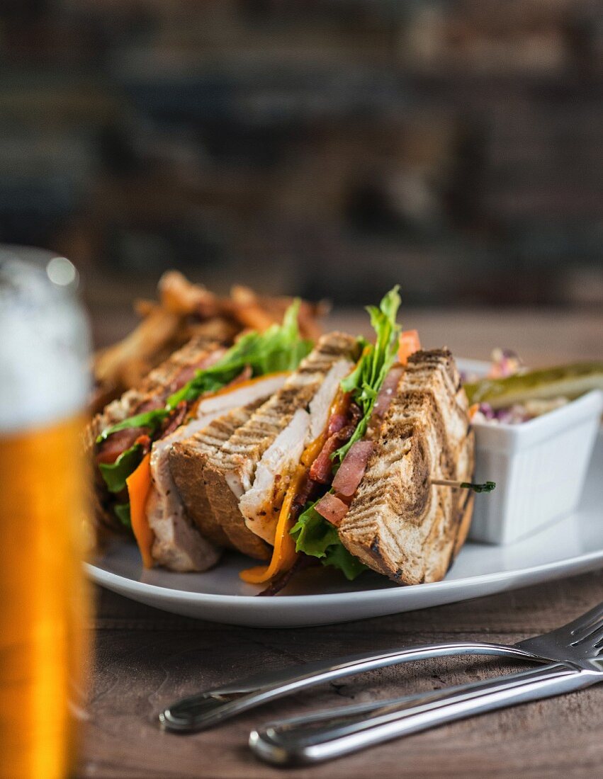 Club-Sandwich mit Marmor-Roggenbrot, dazu Krautsalat und Bier