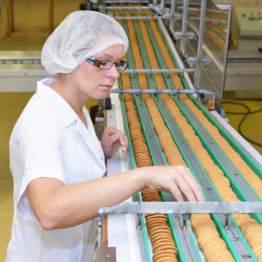 A woman checking biscuits on a conveyor belt in a baking factory