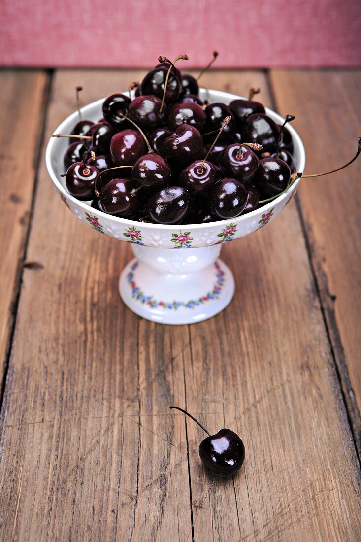 Cherries in a bowl on a wooden table with one cherry in the foreground