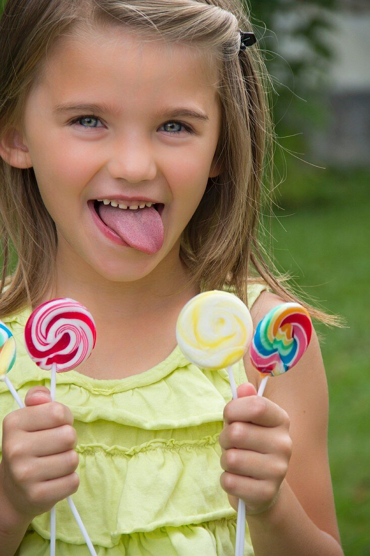 A little girl holding three lollipops