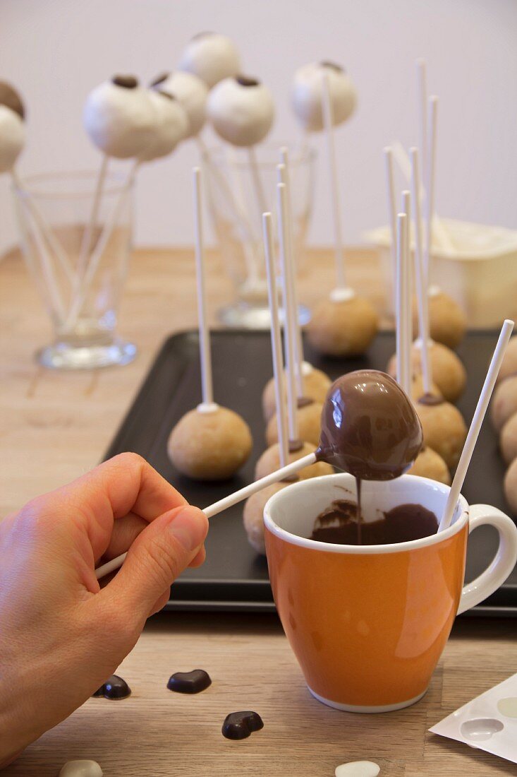 A woman dipping cake pops into chocolate glaze
