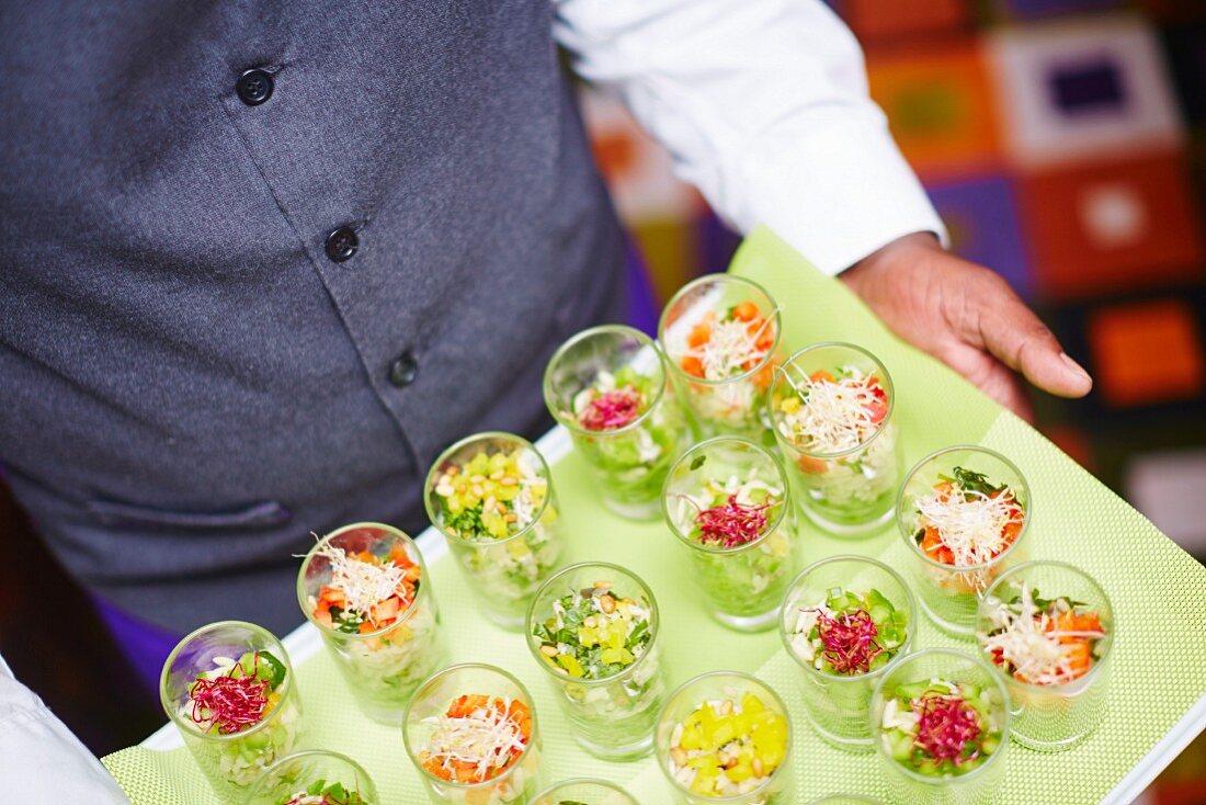 A waiter carrying a tray of individual salads in glasses