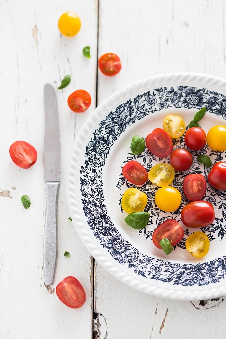 Gelbe und rote Kirschtomaten mit Basilikum auf Teller