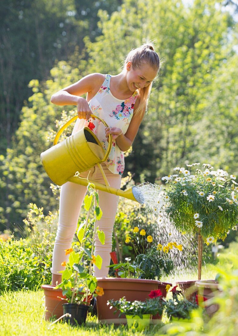 Laughing teenage girl watering potted plants in garden