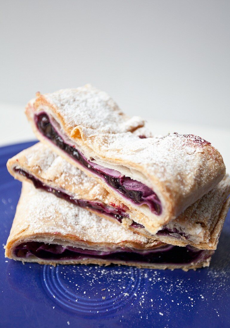 A stack of three slices of blueberry strudel dusted with icing sugar