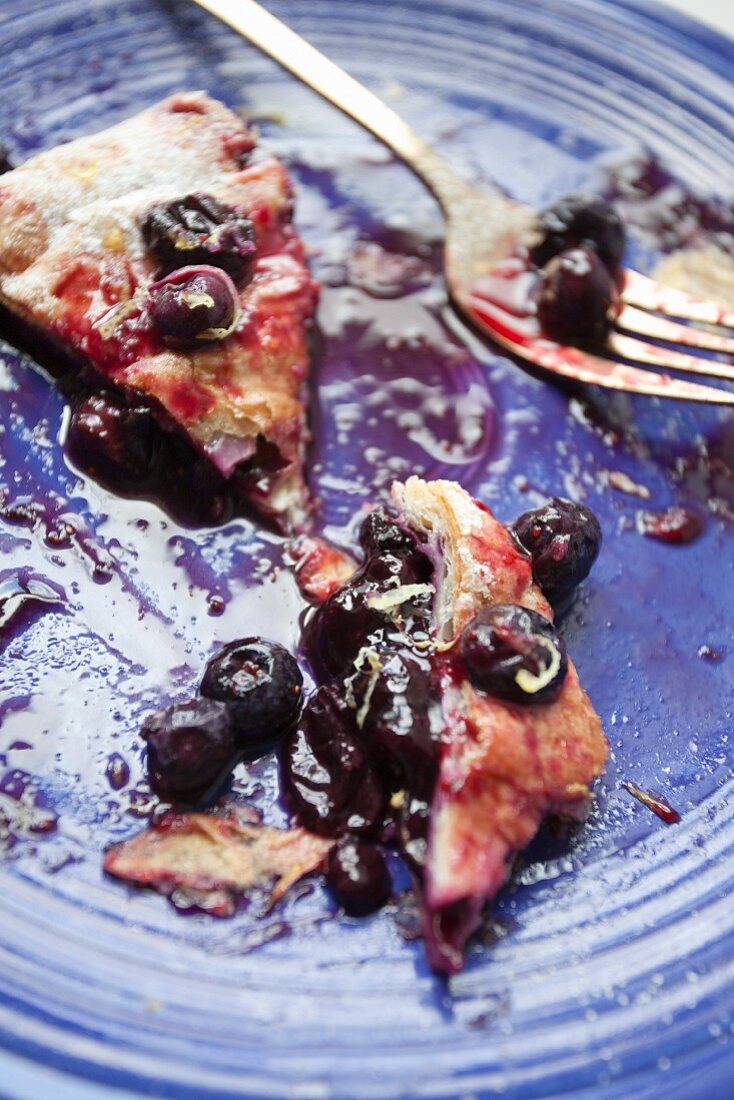 A slice of blueberry strudel with blueberry sauce, half eaten