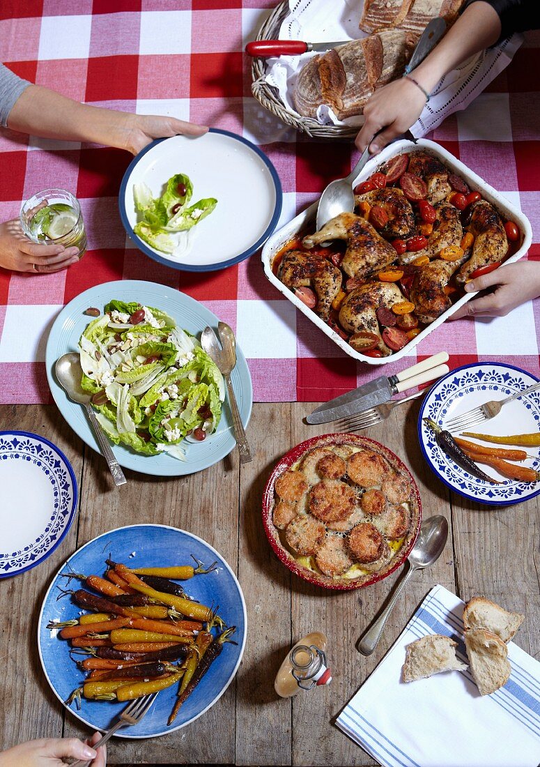 A rustic table laid with herb chicken, sweet potato gratin and salad