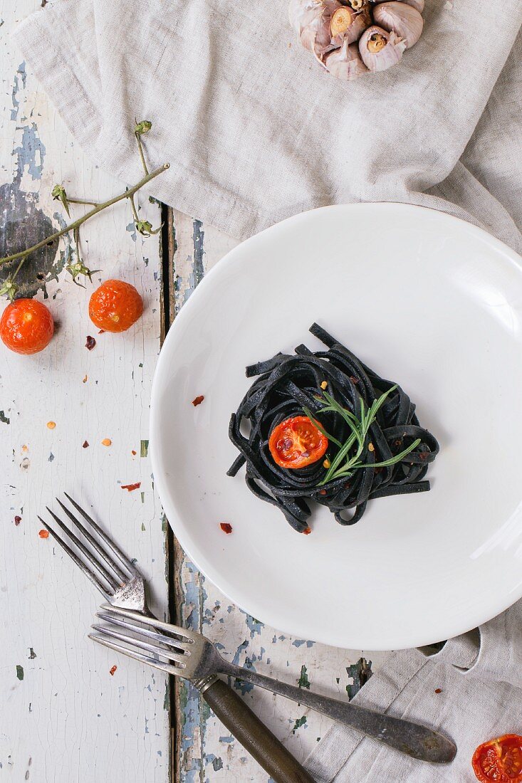 Black tagliolini with baked tomatoes and garlic on old wooden table