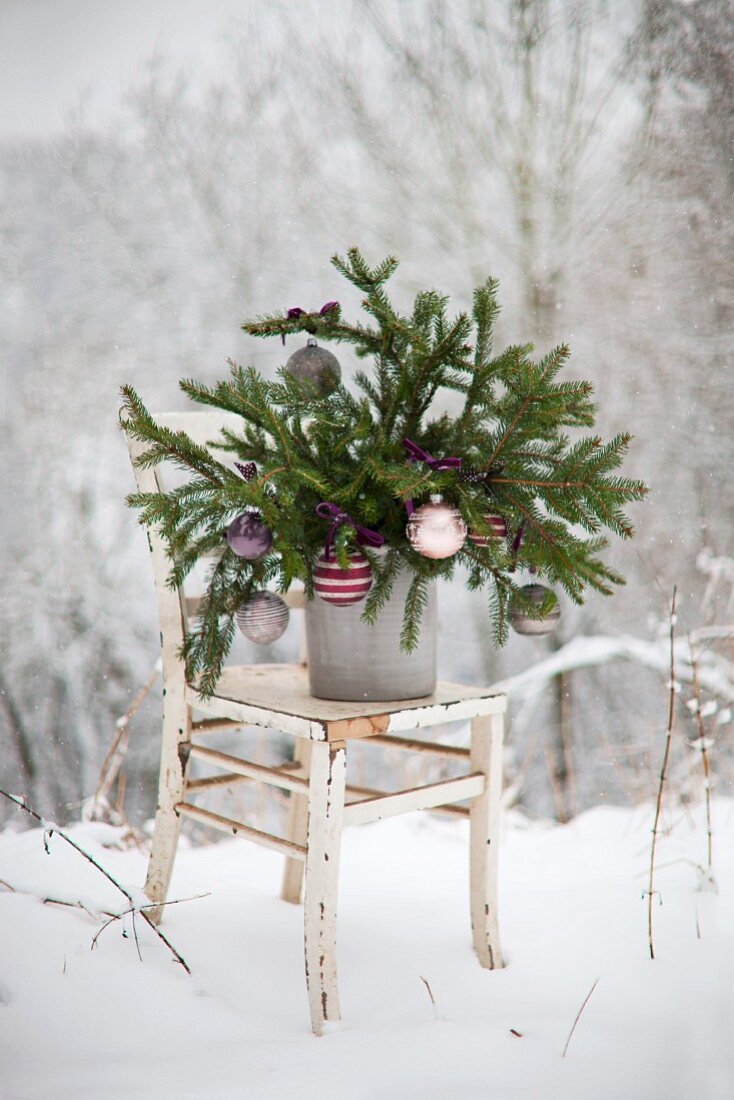 Spruce branches decorated with Christmas baubles on shabby-chic chair in snowy landscape