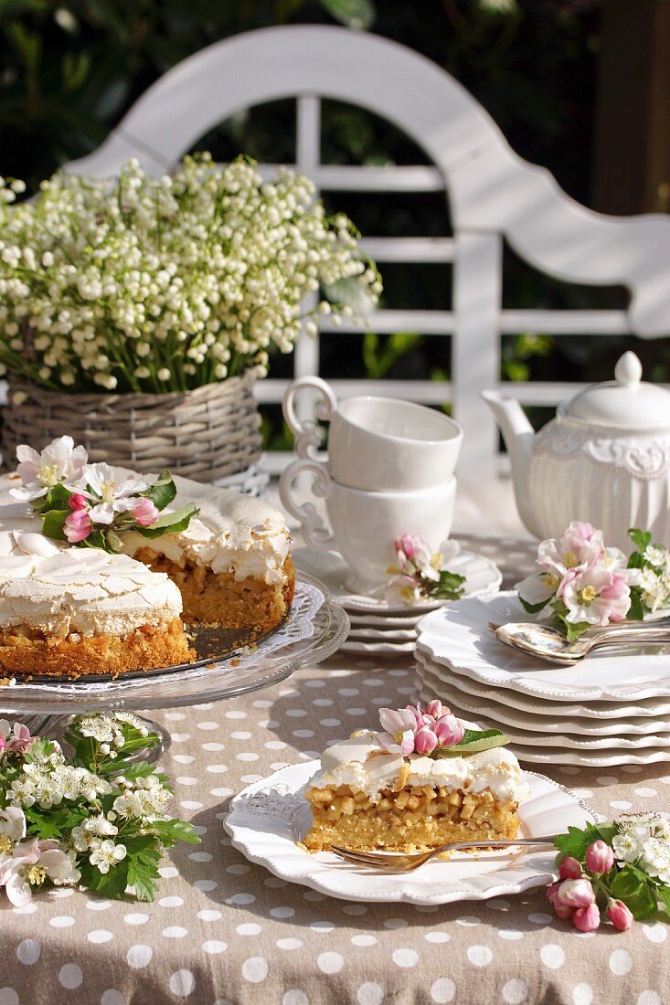 Apple cake with meringue topping, coffee service and opulent bouquet of lily-of-the-valley on sunny table outdoors