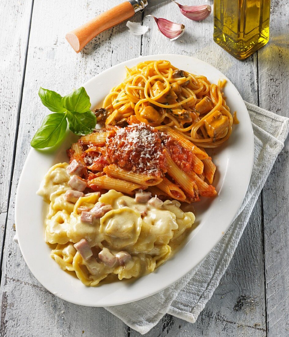 Three pasta dishes on an oval platter garnished with basil