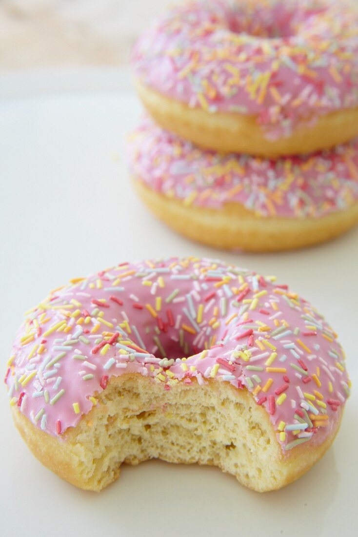 Pinkfarbene Doughnuts mit Zuckerstreuseln, eins angebissen