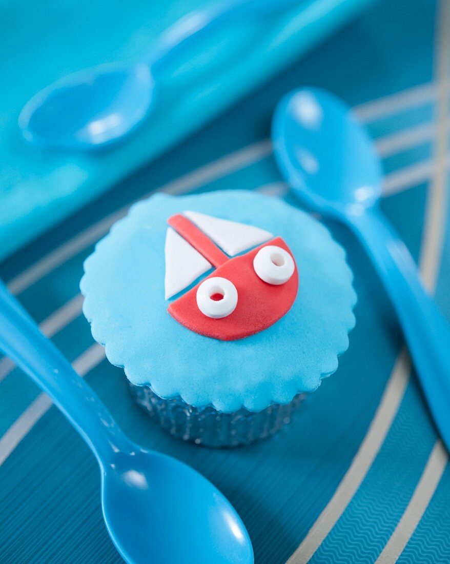 A cupcake decorated with a fondant boat on a blue background