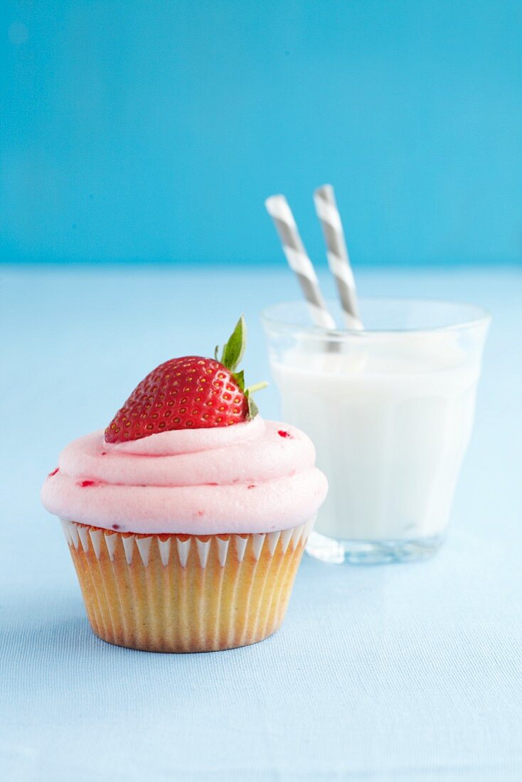 A strawberry cupcake served with a glass of milk