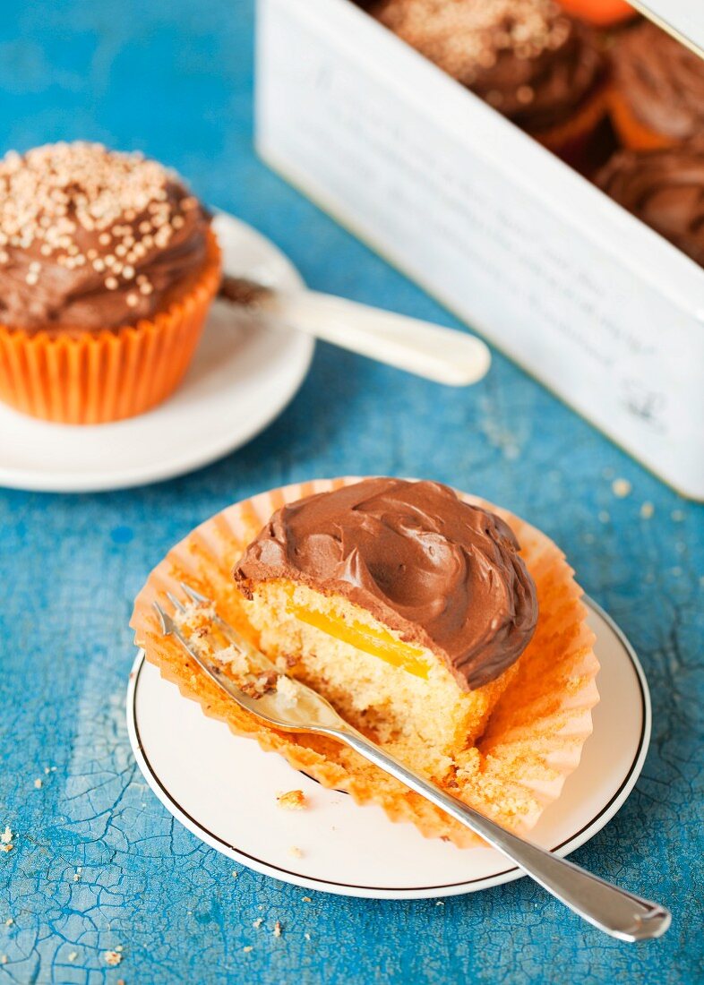 A cupcake filled with orange jelly and topped with chocolate ganache