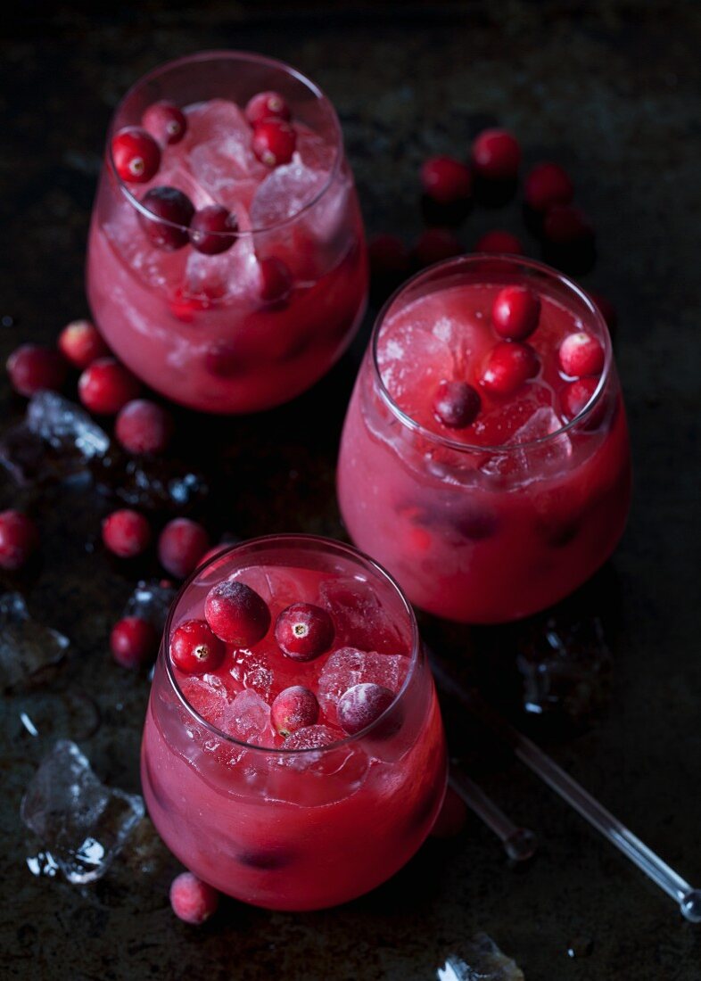 Three whiskey and cranberry cocktails with ice cubes