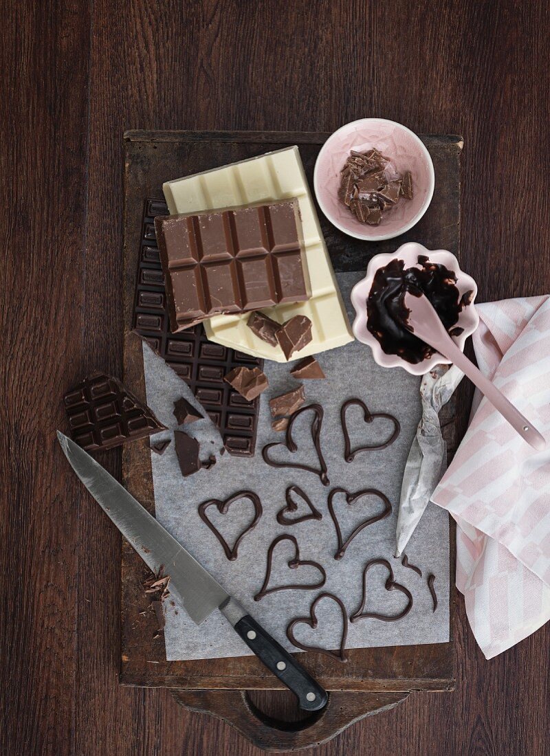 Verschiedene Schokoladentafeln, geschmolzene Schokolade und Kuvertüreherzen