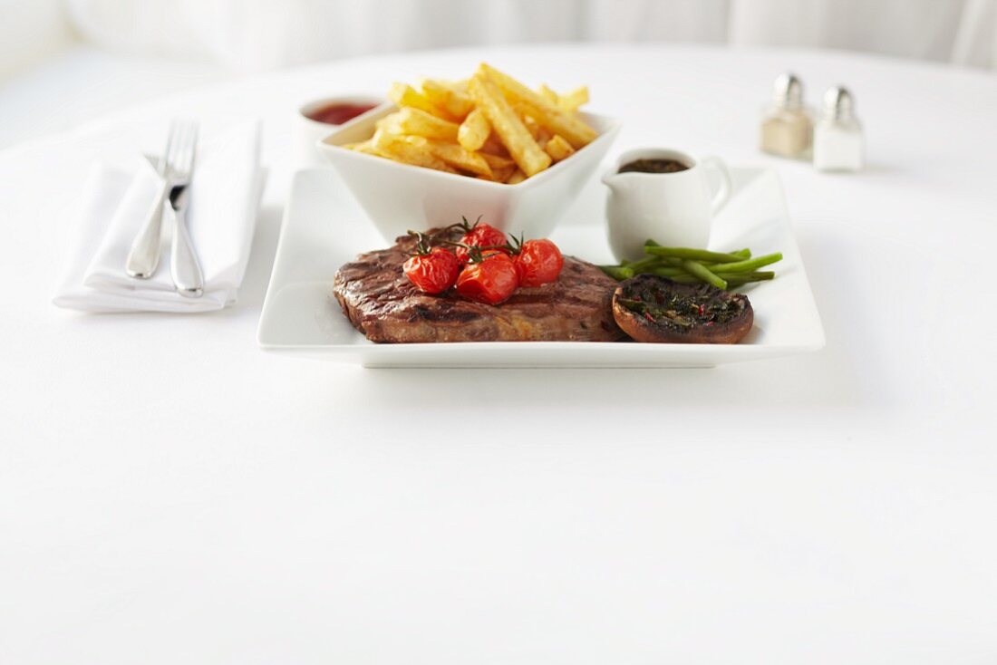 Steak with chips, pepper sauce, grilled tomatoes and mushrooms
