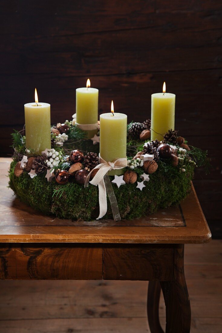 Rustic Advent wreath with four lit green candles decorated with walnuts, moss and pine cones
