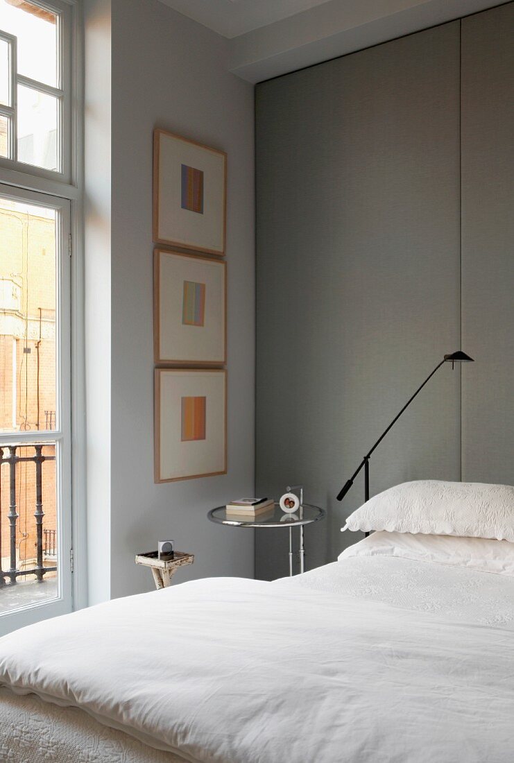 Bett mit weisser Bettwäsche, an Wand grau bezogene, raumhohe Paneelen in traditionellem elegantem Ambiente