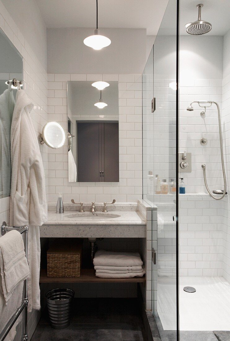 Marble washstand below mirror on white-tiled wall next to glass shower screen in small bathroom