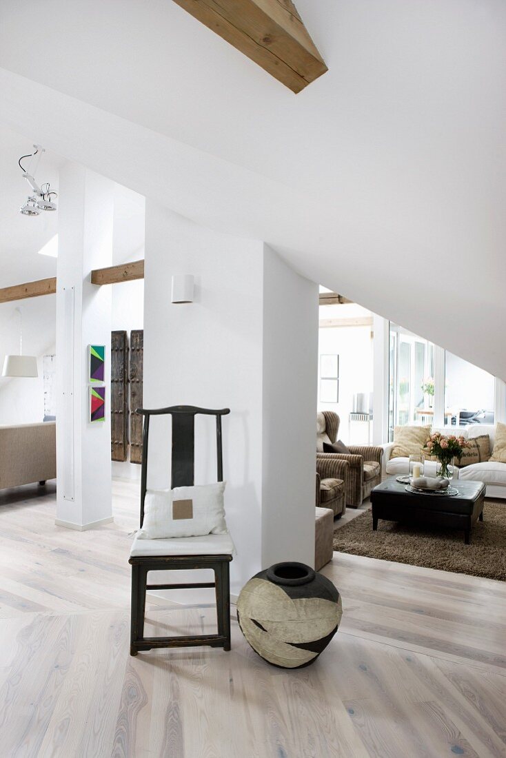 Antique dark chair and floor vase on pale wooden floor against pillar ni front of lounge area in converted attic