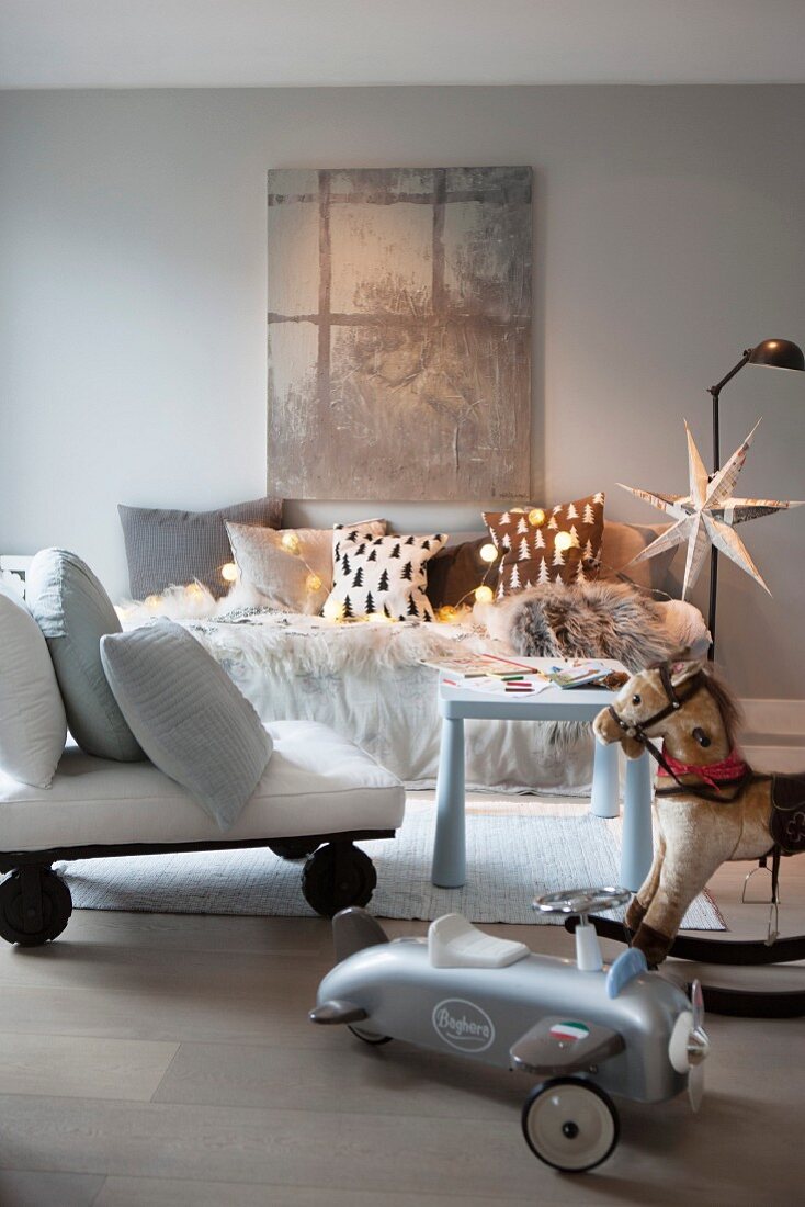 Festively decorated interior with sofa, chaise on large castors, rocking horse and ride-on toy car