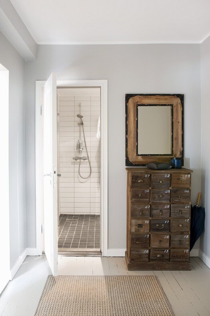 Vintage apothecary cabinet and mirror against pale grey wall next to open bathroom door