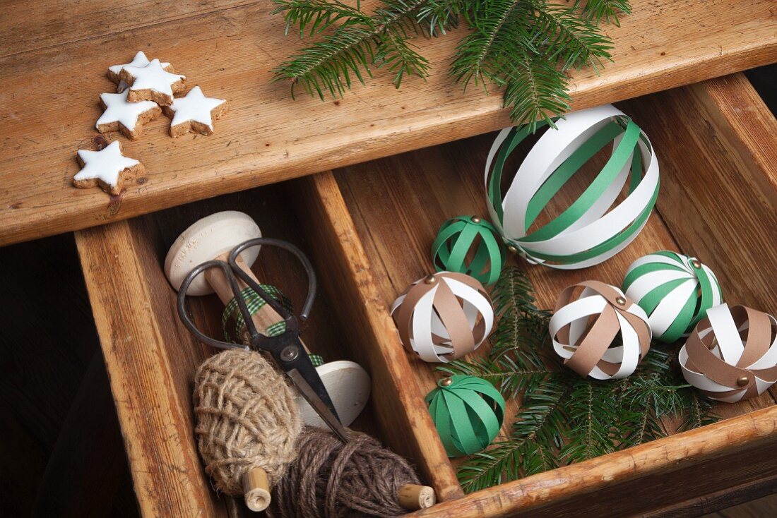 Hand-crafted baubles made from paper strips and bobbins of pale brown cord festively arranged with fir twigs and cinnamon stars