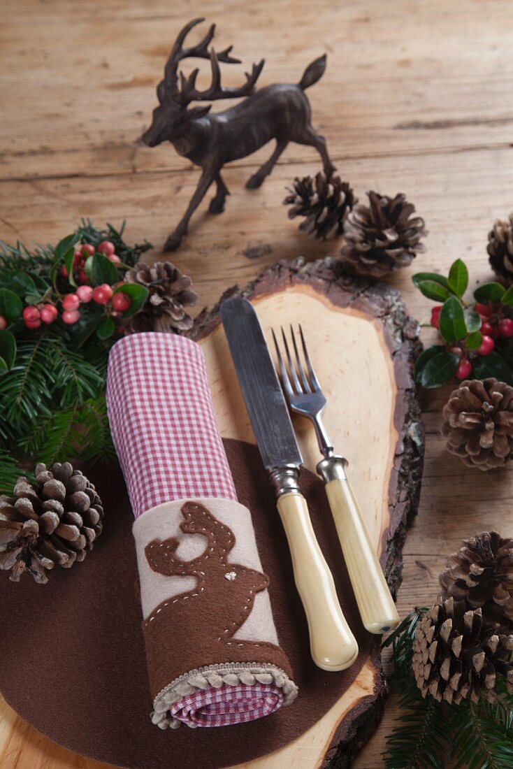 Rustic wooden board and hand-crafted felt napkin ring with appliqué stag motif on festively decorated wooden table