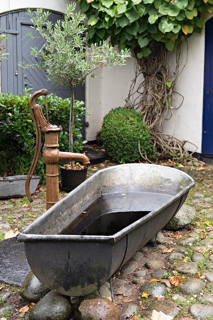 Vintage zinc bathtub next to pump in cobbled courtyard