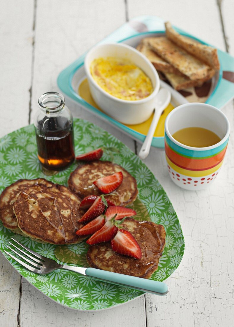 Pancakes, Erdbeeren, Ahornsirup, Eier und Toast zum Frühstück