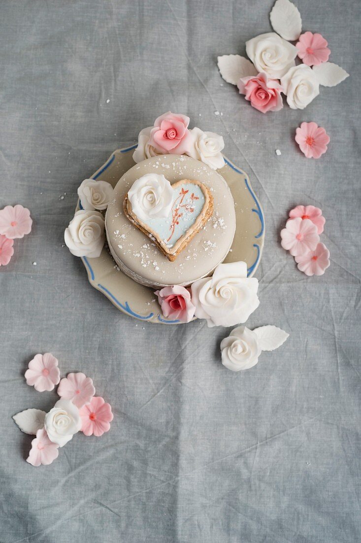 A cake decorated with fondant icing sugar, heart-shaped biscuit and sugar roses