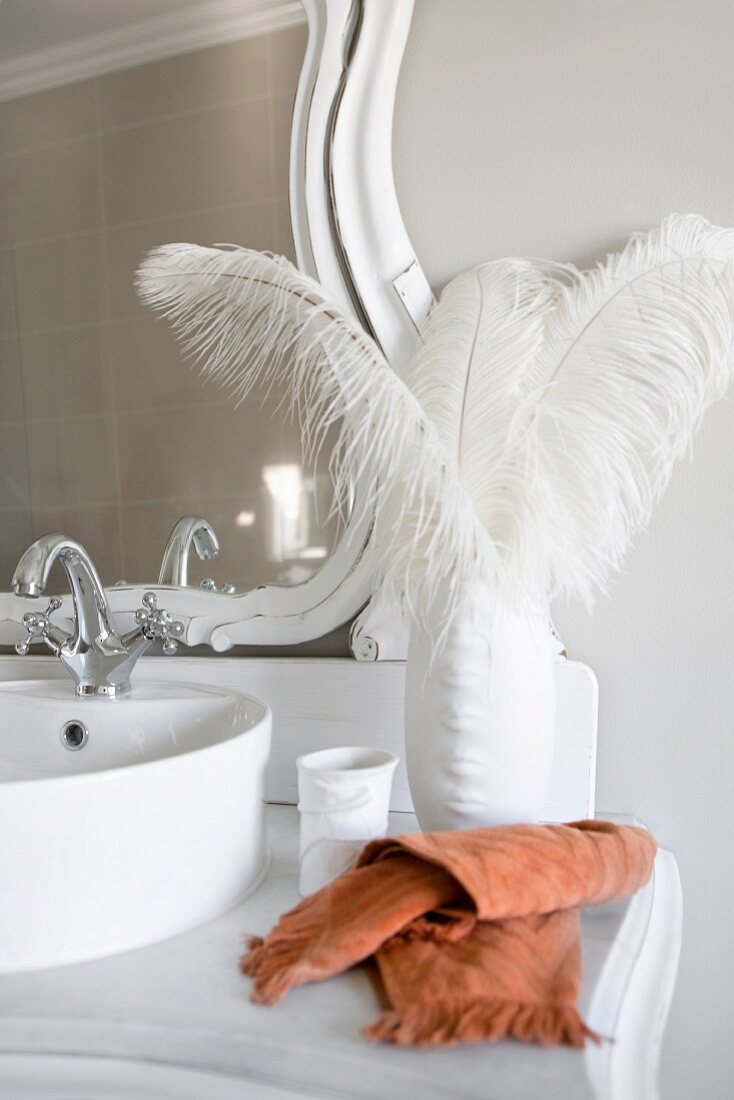 White ostrich feathers in elegant porcelain vase on vintage washstand with vanity mirror