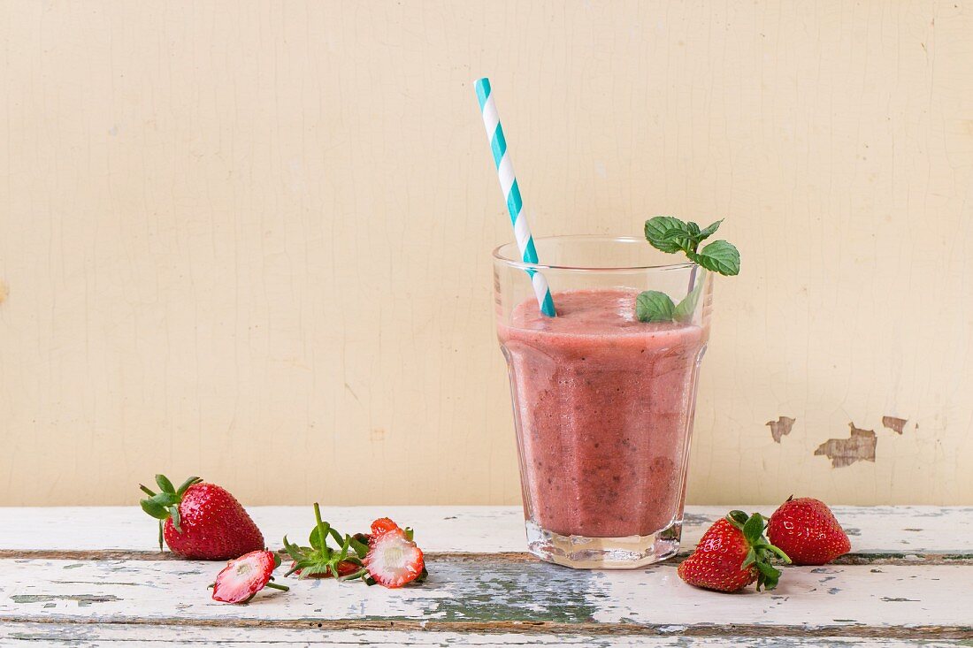A glass of strawberry smoothie with chia seeds, fresh strawberries and mint