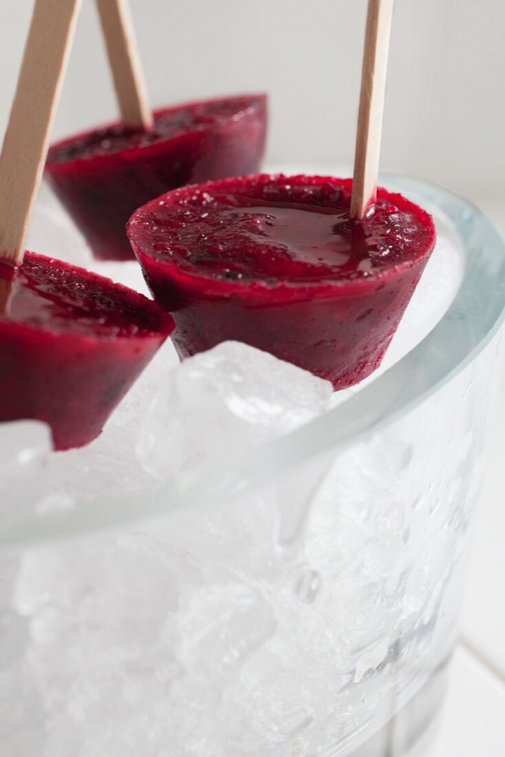 Three grapefruit and blackberry ice lollies in a bowl of ice