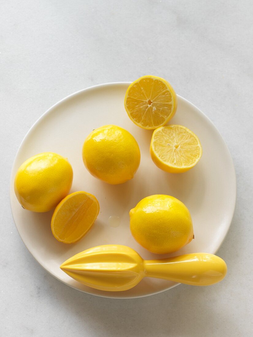 Mehrere Meyer Zitronen, ganz und halbiert, mit Presse