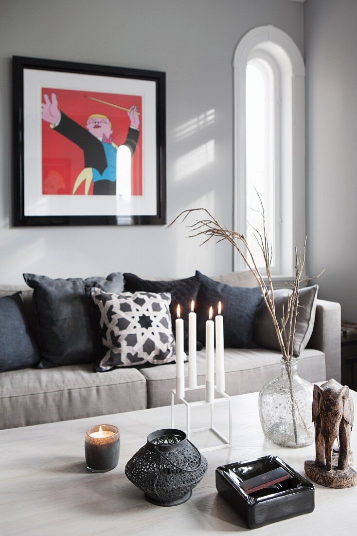 Kerzenhalter mit brennenden Kerzen und Windlichter auf Tisch, Sofa mit Kissen, an grauer Wand modernes Bild, in traditionellem Ambiente